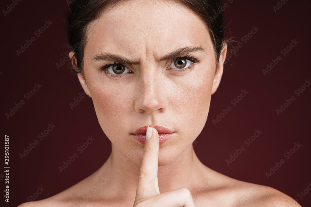 Naklejka premium Image of frowning shirtless woman holding finger at her lips