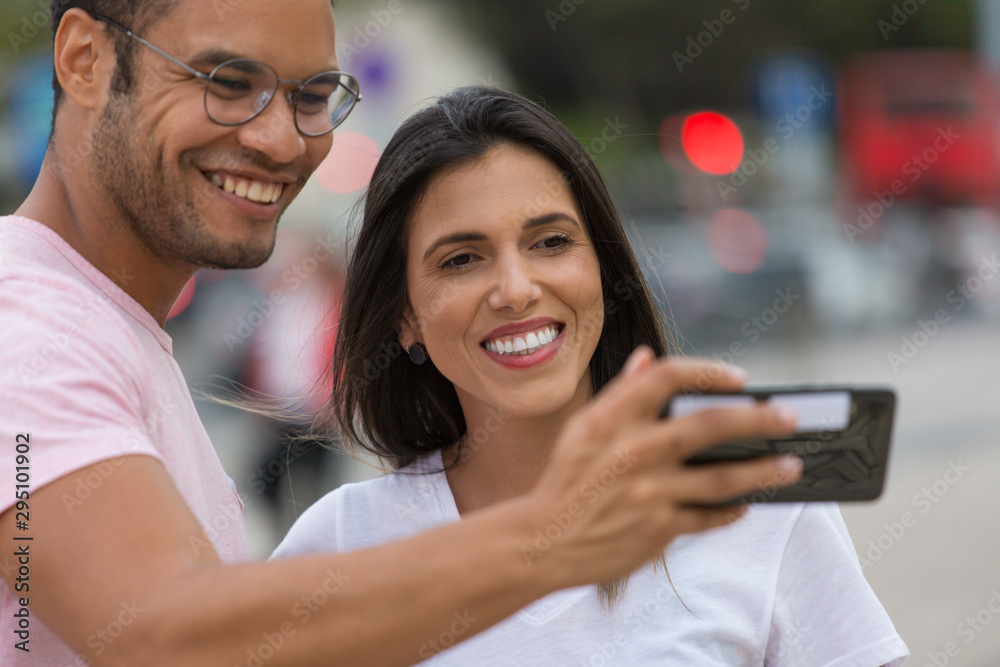 Happy multiracial friends taking self portrait with smartphone. Cheerful couple posing for selfie on street. Concept of self portrait Happy multiracial friends taking self portrait with smartphone. Cheerful couple posing for selfie on street. Concept of self portrait