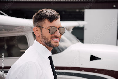 bearded pilot in formal wear and sunglasses smiling near plane © LIGHTFIELD STUDIOS