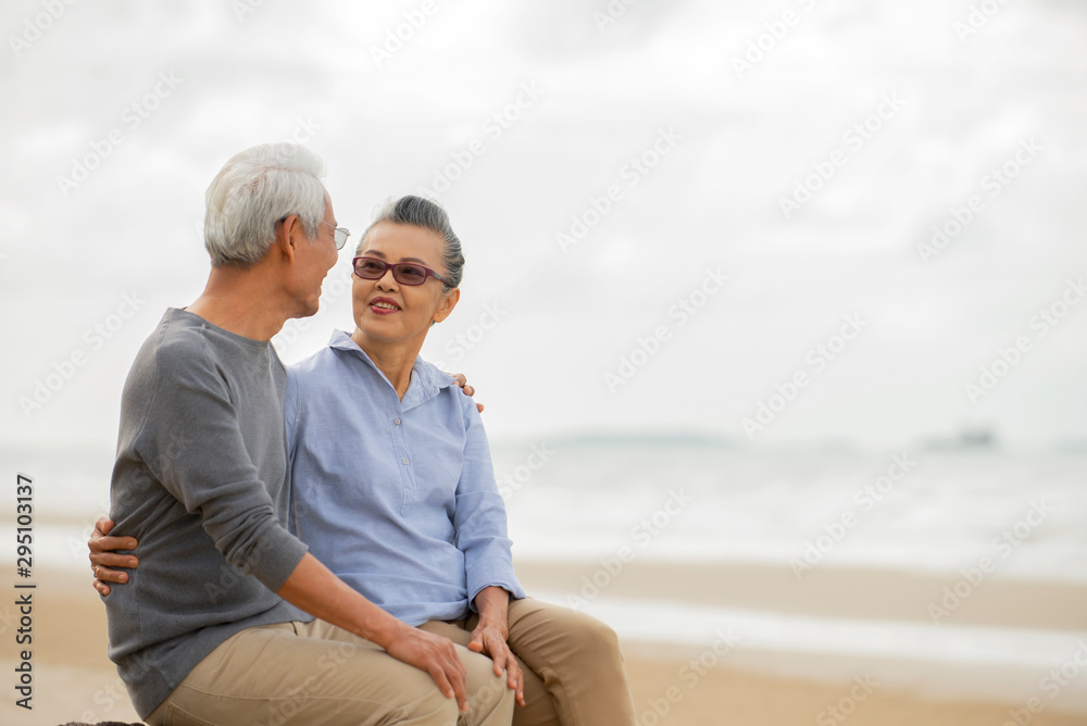 Happy asian senior couple  have fun and enjoy at the beach, senior man and woman hugging while sitting on the beach Retirement Lifestyle Healthy  Travel Vacation Concept