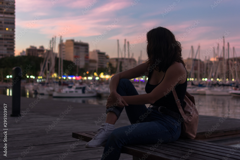 Young woman is sitting on a bench in a harbor Young woman is sitting on a bench in a harbor