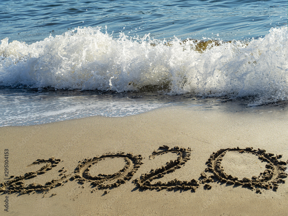 Fototapeta premium 2020 written by hand on the sand beach with beautiful wave and clear blue sea. Handwritten lettering numbers 2020 on sea shore. New Years concept.