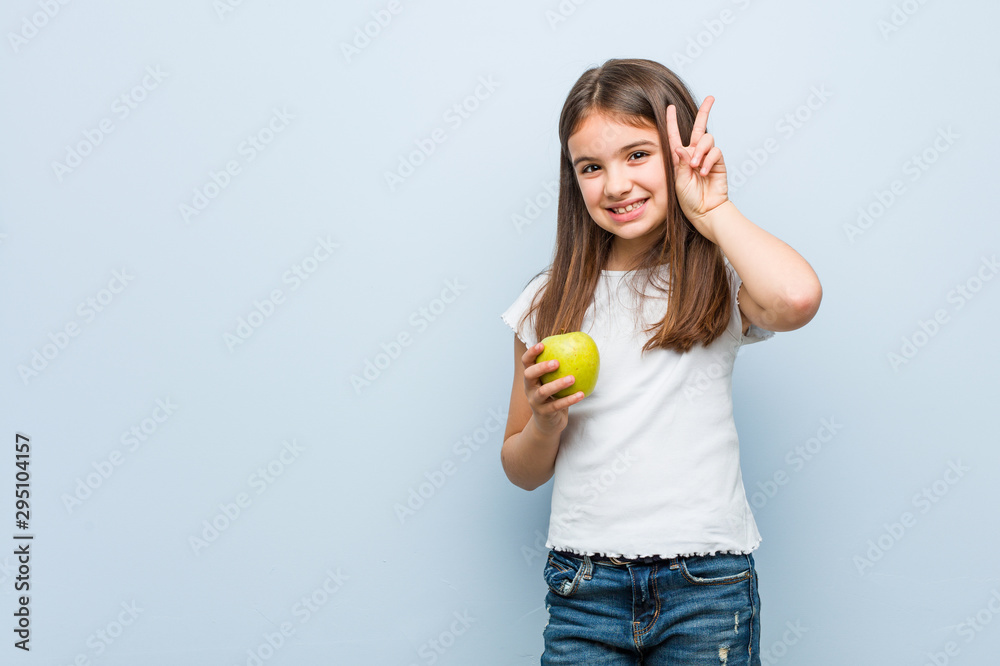 Little caucasian girl holding a green apple showing victory sign and smiling broadly. Little caucasian girl holding a green apple showing victory sign and smiling broadly.