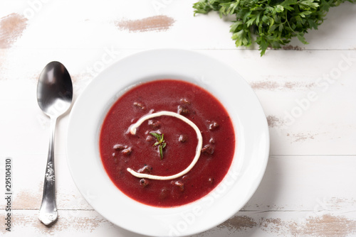 Delicious beet soup with sour cream in a white plate on white wooden table background. Soft light. Traditional Ukrainian Russian borscht beetroot soup