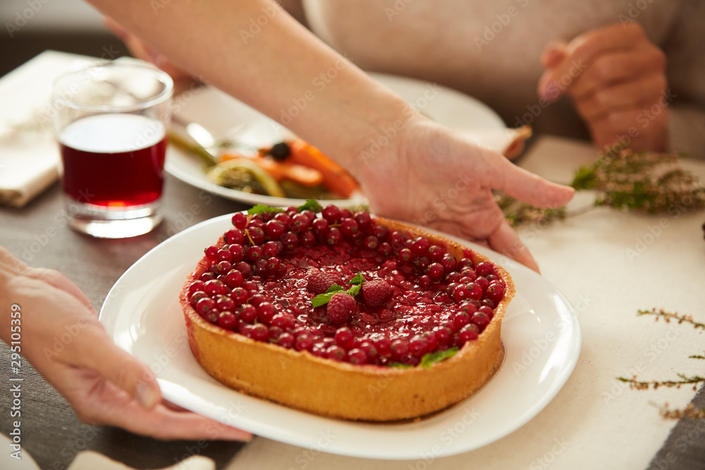 Close-up of woman putting berry sweet pie on the table during holiday dinner