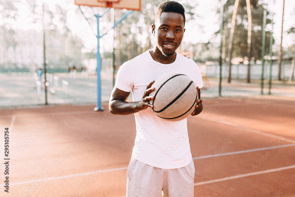 Sporty young African American standing on the court at dawn with a basketball Sporty young African American standing on the court at dawn with a basketball