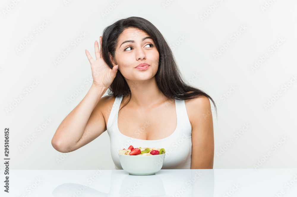 Young hispanic woman eating a fruit bowl trying to listening a gossip. Young hispanic woman eating a fruit bowl trying to listening a gossip.