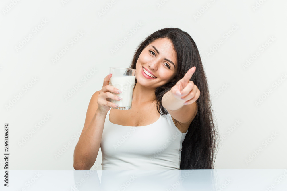 Young hispanic woman holding a glass of milk cheerful smiles pointing to front. Young hispanic woman holding a glass of milk cheerful smiles pointing to front.