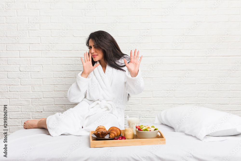 Young curvy woman taking a breakfast on the bed rejecting someone showing a gesture of disgust.