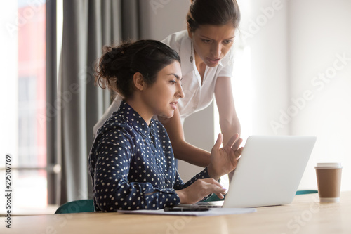 Diverse female mentor and intern talking pointing on laptop