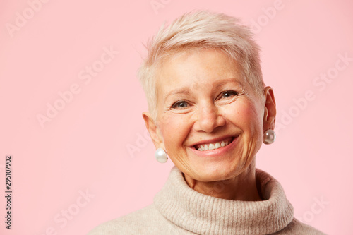 Portrait of beautiful happy mature woman smiling at camera over pink background