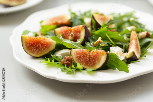 Salad with arugula, figs, cheese, walnut and honey. Autumn salad with figs and cheese on a white plate.