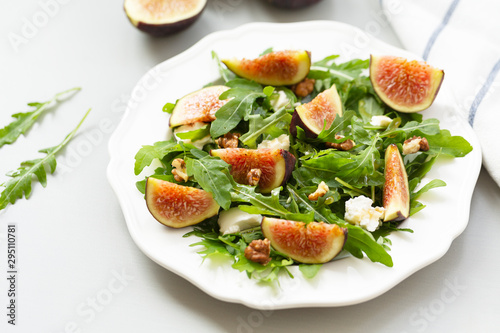 Salad with arugula, figs, cheese, walnut and honey. Autumn salad with figs and cheese on a white plate.