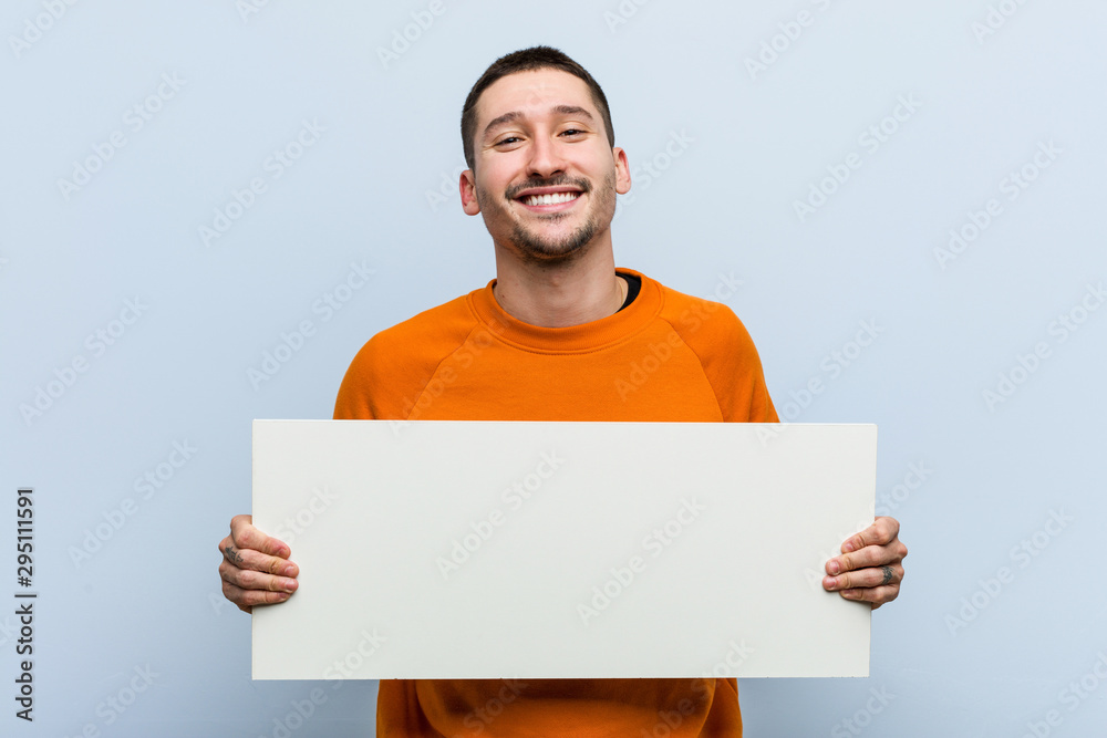 Young caucasian man holding a placard happy, smiling and cheerful. - obrazy, fototapety, plakaty 