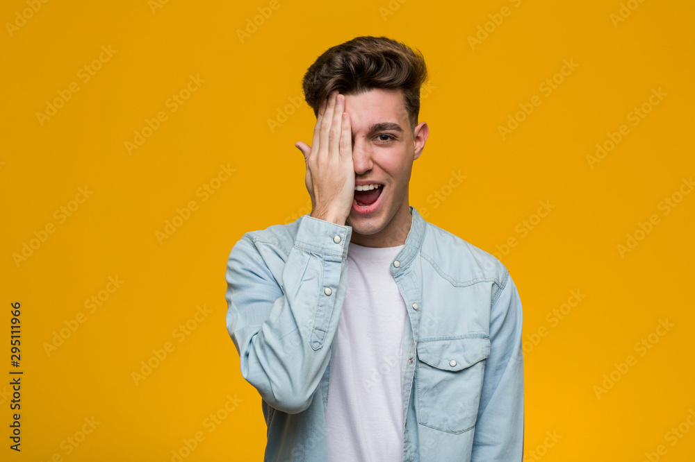 Young handsome student wearing a denim shirt having fun covering half of face with palm. Young handsome student wearing a denim shirt having fun covering half of face with palm.