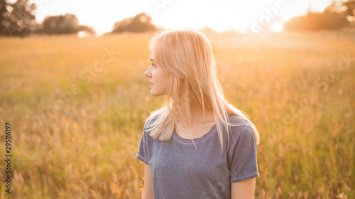 Beautiful blonde young woman walking on the field at sunset