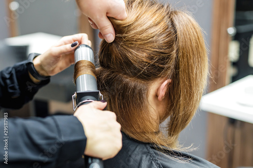 Close up photo of hairdresser is curling hair for woman in beauty salon. Concept of creating hairstyle.
