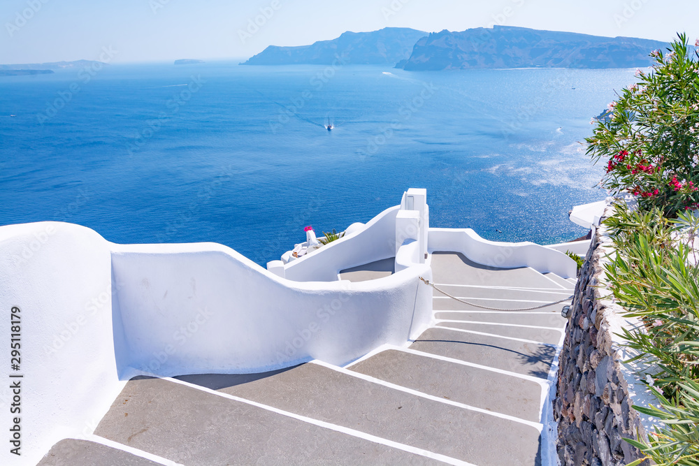 Fototapeta premium Tradycyjna wąska ulica ze schodami prowadzącymi do morza w miejscowości Oia, wyspa Santorini, Grecja. Piękny letni krajobraz, widok na morze