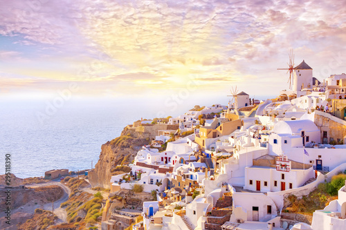 Beautiful view of picturesque village of Oia with traditional white architecture and windmills in Santorini island in Aegean sea at sunset, Greece. Scenic travel background.