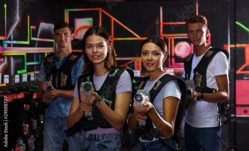 Smiling young women standing with guns during laser tag game with guys
