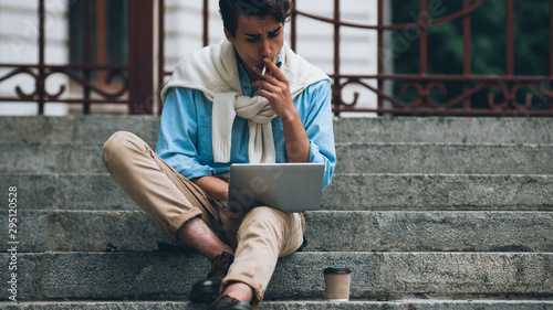 Modern lifestyle. Online remote job. Business man sitting on street with laptop working smoking.