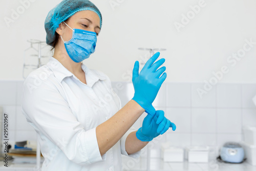 Fototapet A nurse in a white coat puts on rubber gloves before a medical procedure in a bright handling room