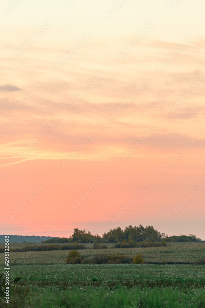 Pink clouds on a red sky during sunrise over a meadow in the countryside