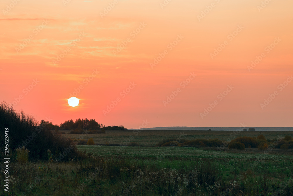 Sun disc on a red sky during sunrise over a road in the countryside.