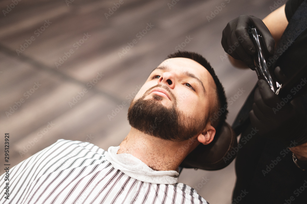 Fototapeta premium Shaving a beard in a barbershop with a dangerous razor. Barber Shop Beard Care. Drying, cutting, cutting a beard. Selective focus.