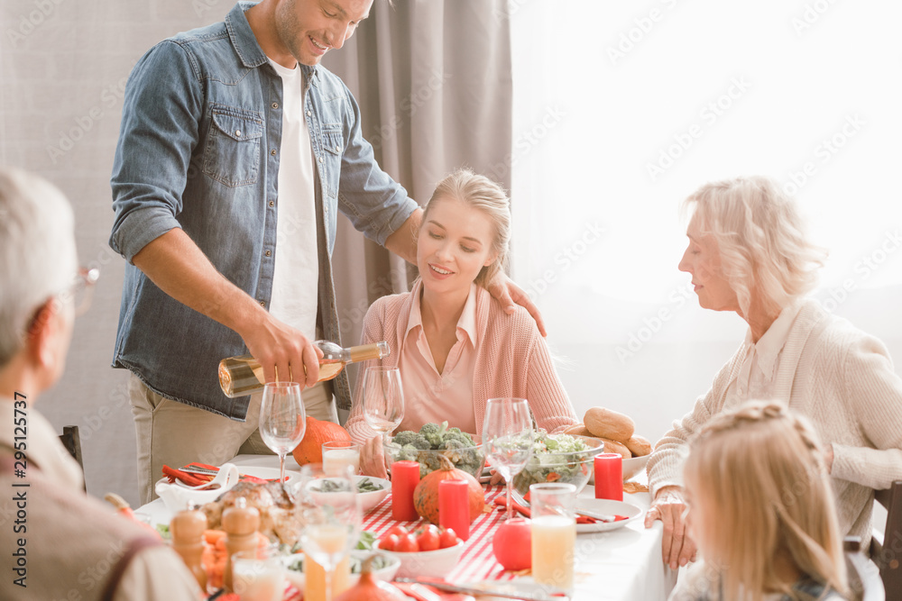 family members sitting at table and smiling father pouring wine in Thanksgiving day