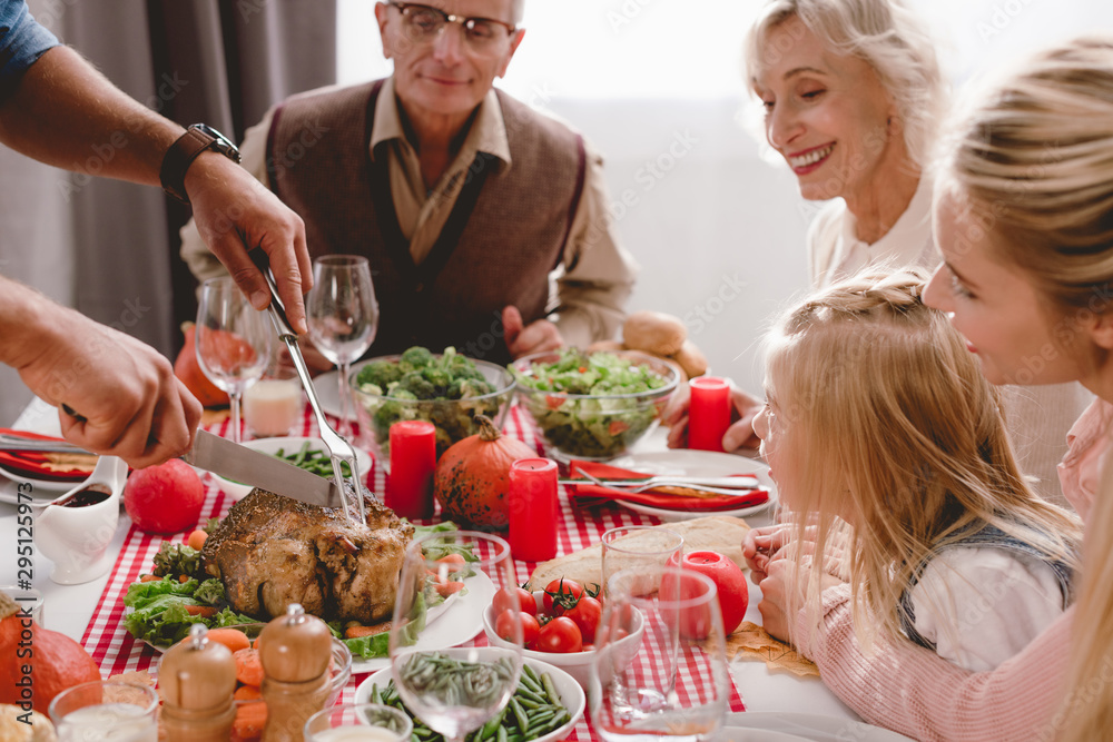 cropped view of family members sitting at table and father cutting tasty turkey in Thanksgiving day cropped view of family members sitting at table and father cutting tasty turkey in Thanksgiving day