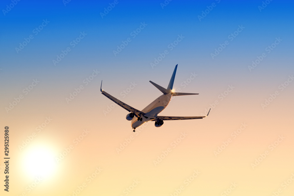 Modern airplane flying against sunset sky background Passenger aircraft landing at sunrise Commercial plane taking off towards setting sun Business jet arriving with landing gear down Aerial view