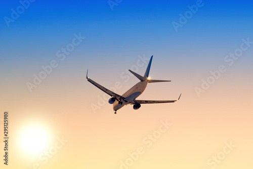 Modern airplane flying against sunset sky background Passenger aircraft landing at sunrise Commercial plane taking off towards setting sun Business jet arriving with landing gear down Aerial view