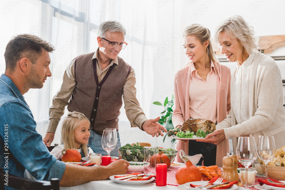 family members sitting at table and holding plate with turkey in Thanksgiving day family members sitting at table and holding plate with turkey in Thanksgiving day