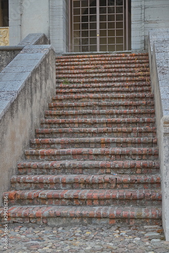 An ancient stone staircase, the steps are lined with bricks. The staircase leads to the gate, which is closed with bars. Europe, Italy © blisser