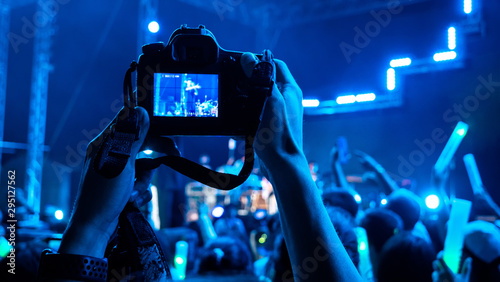 Photographer taking picture with camera at a festival concert with crowd people raised hands and attending a concert. Blue black light by stage lights. Summer music festival concept.