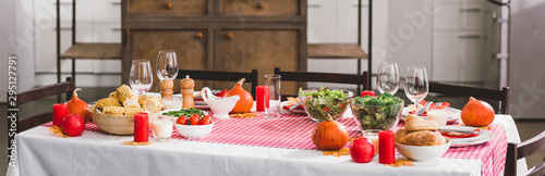 panoramic shot of table with salad, glasses, candles, vegetables, pepper mill, corn, salt mill and pumpkins in Thanksgiving day