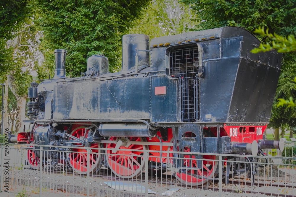 Naklejka premium Vintage black and red steam locomotive, which stands in an open area behind the fence (in the park)