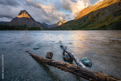 Two big branches on the beach and tree rocks at Two Medicine Lake with the view of the Mountains at sunrise in the background, Two Medicine Lake, Montana. photo