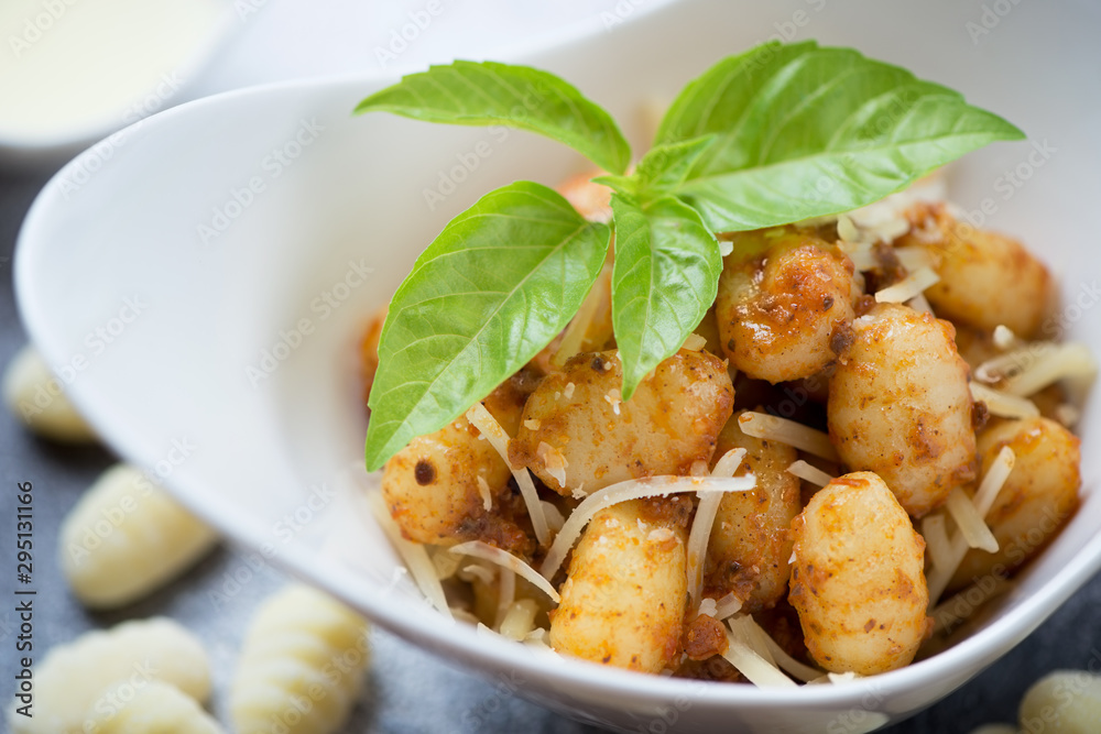 Potato gnocchi served with sun dried tomatoes pesto, parmesan and fresh green basil, close-up, selective focus