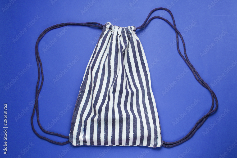 Striped beach backpack on blue background. Top view - obrazy, fototapety, plakaty 