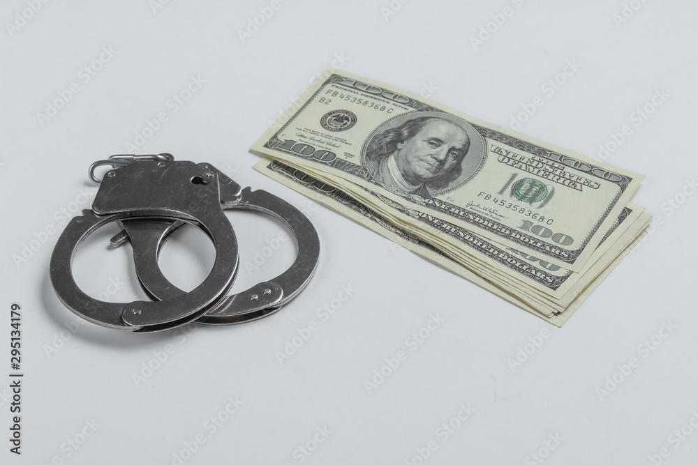 Steel handcuffs and one hundred dollar bills on a white background. Crime, corruption concept Steel handcuffs and one hundred dollar bills on a white background. Crime, corruption concept