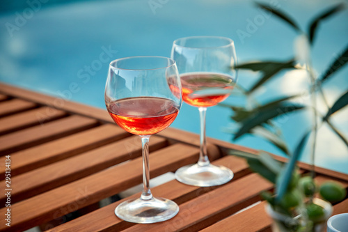 two glasses of rose wine with olives against blue water on a pier..