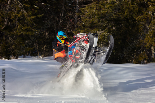 rider in a bright suit on a colorful snowmobile raises snow tubers in a mountain forest. riding a caterpillar heel on a snow motorcycle. snowmobile sports concept, athlete on snowy moto. super quality
