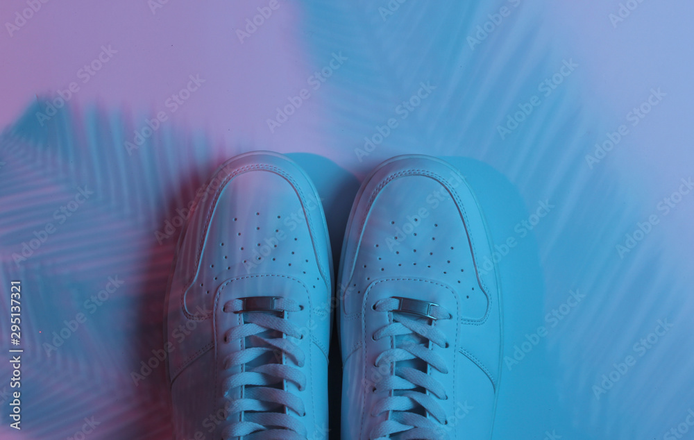 Stylish hister white sneakers on background with shadow from palm leaves. Neon gradient light. Top view