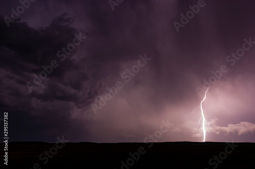 Single bolt of lightning hitting the ground from dramatic purple supercell thunderstorm