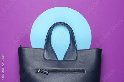 Fashionable leather bag on purple background with blue pastel circle. Top view