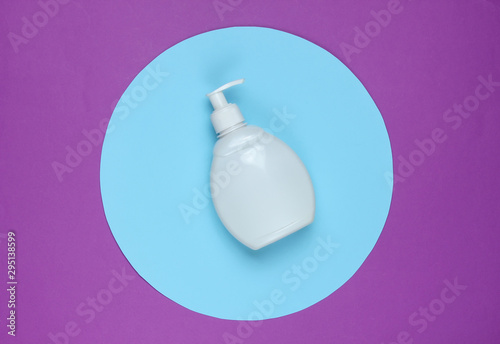 White shampoo bottle on a purple background with a blue pastel circle in the middle. Top view. Minimalistic beauty concept.