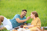 Young man feeding his girlfriend with grape on picnic blanket outdoors