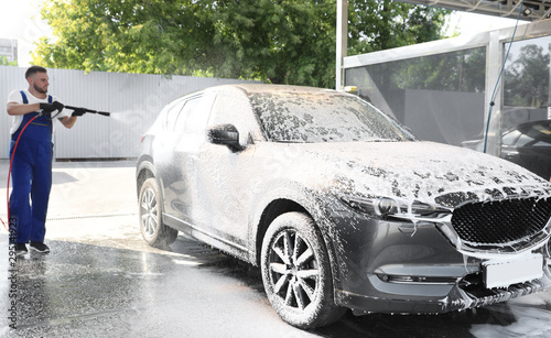 Quadro su tela Young worker cleaning automobile with high pressure water jet at car wash